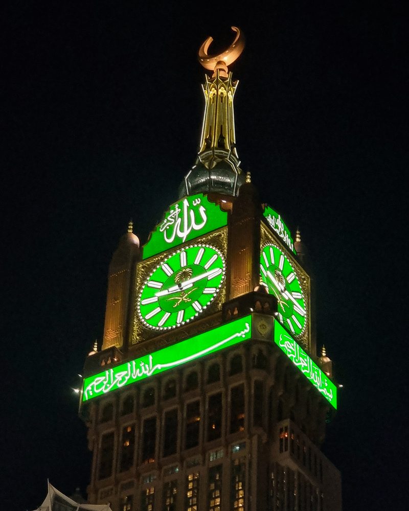 The Abraj al-Bait clock tower lit green at night, beside Masjid al-Haram in Makkah